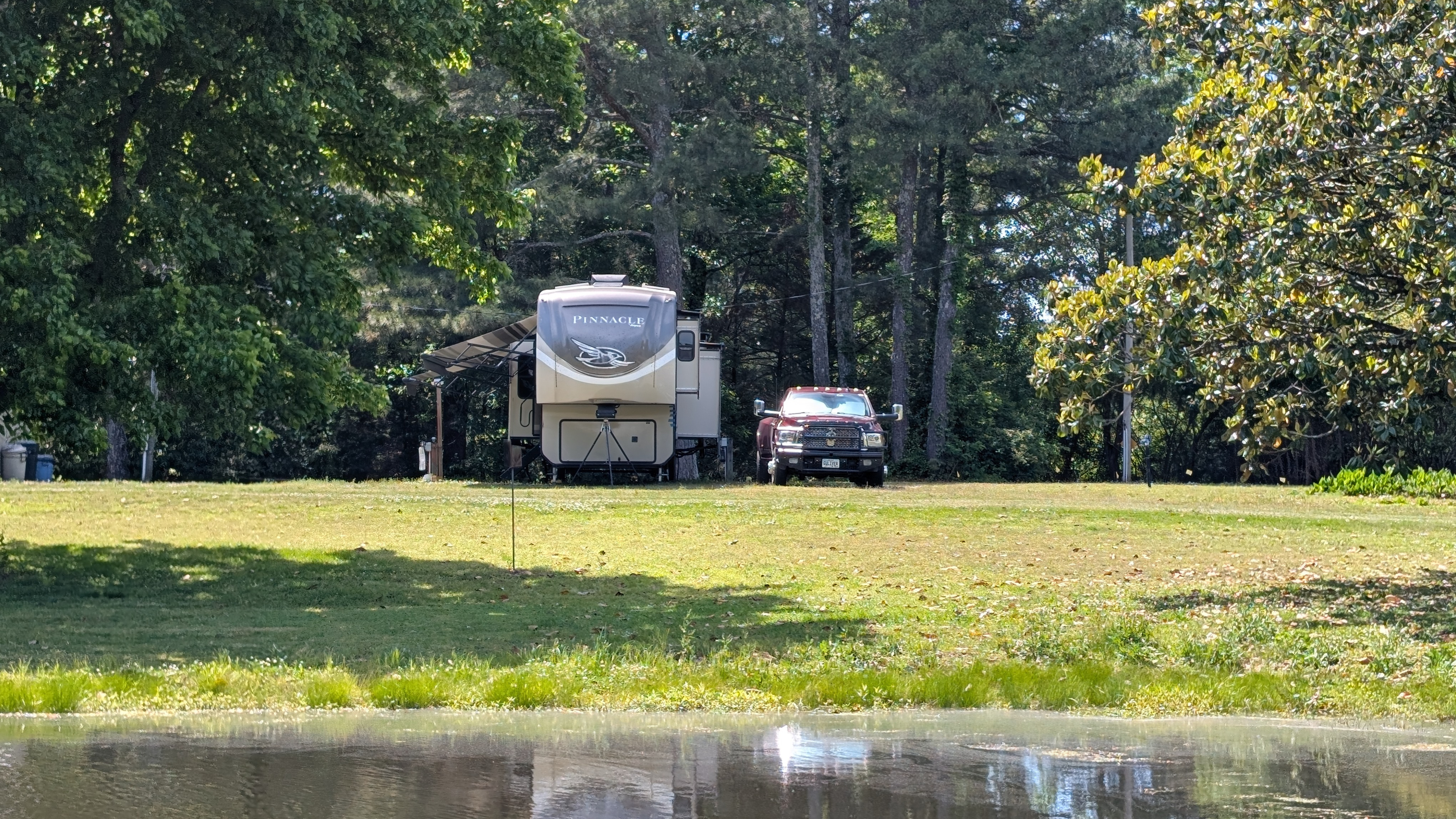 A fifth wheel and truck flanked by trees on the other side of a pond