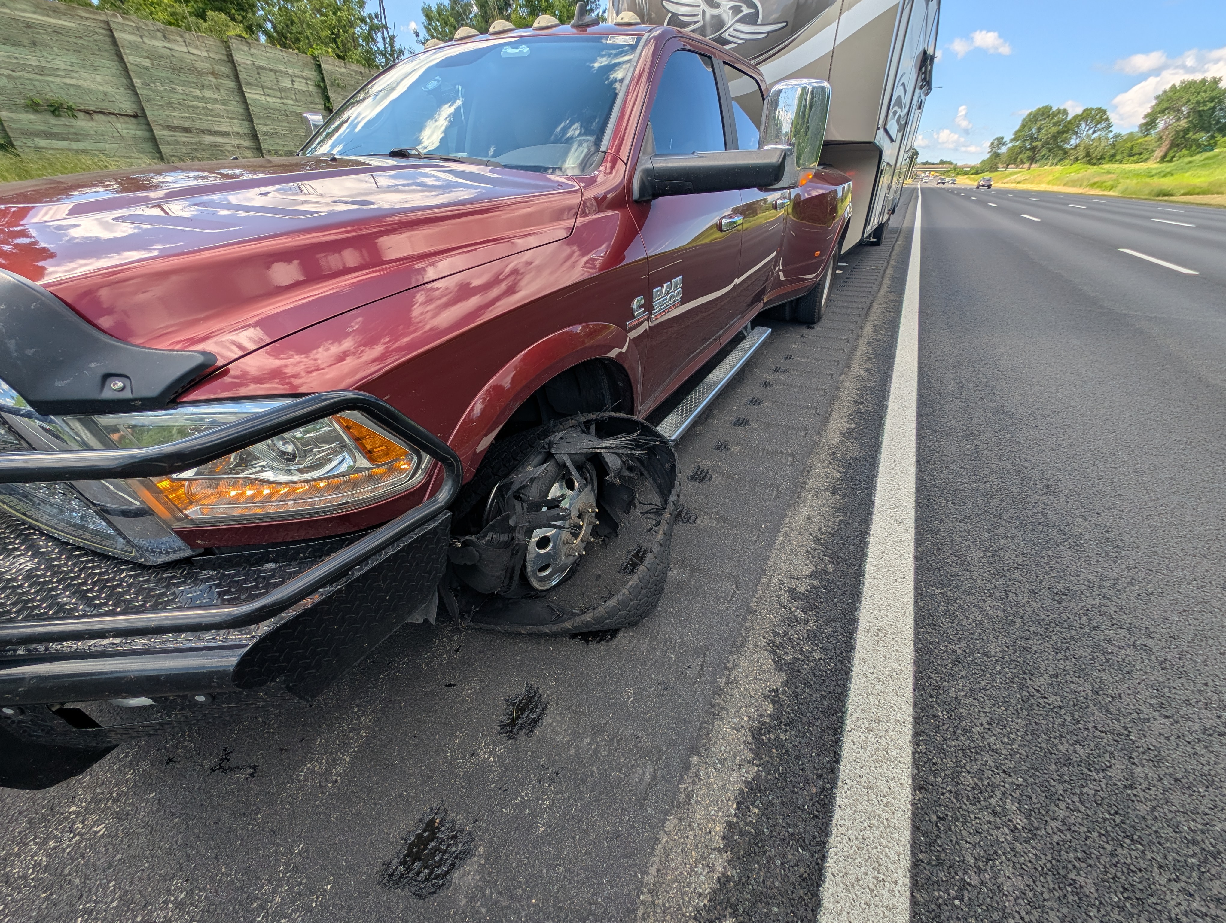 Truck with a flat tire attached to a fifth wheel RV on the side of a freeway