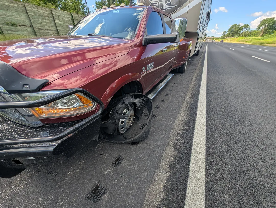 A truck with a flat tire attached to a fifth wheel on the side of a freeway