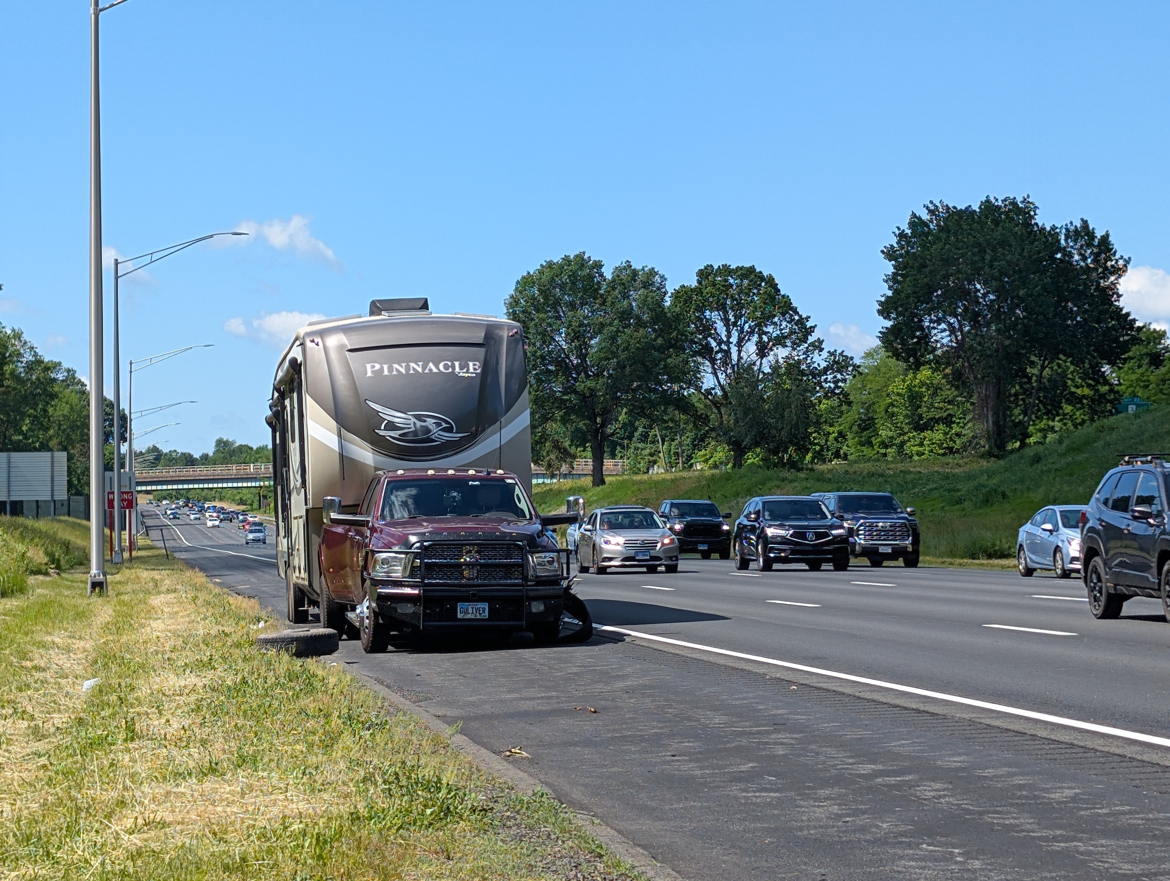 Wide-angle view of a disabled truck and fifth wheel on the side of  busy, four-laned freeway