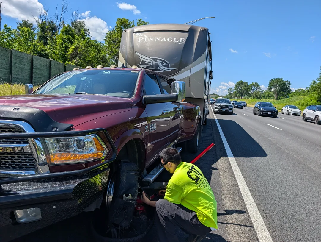 Service tech working on a truck tire on the side of a freeway