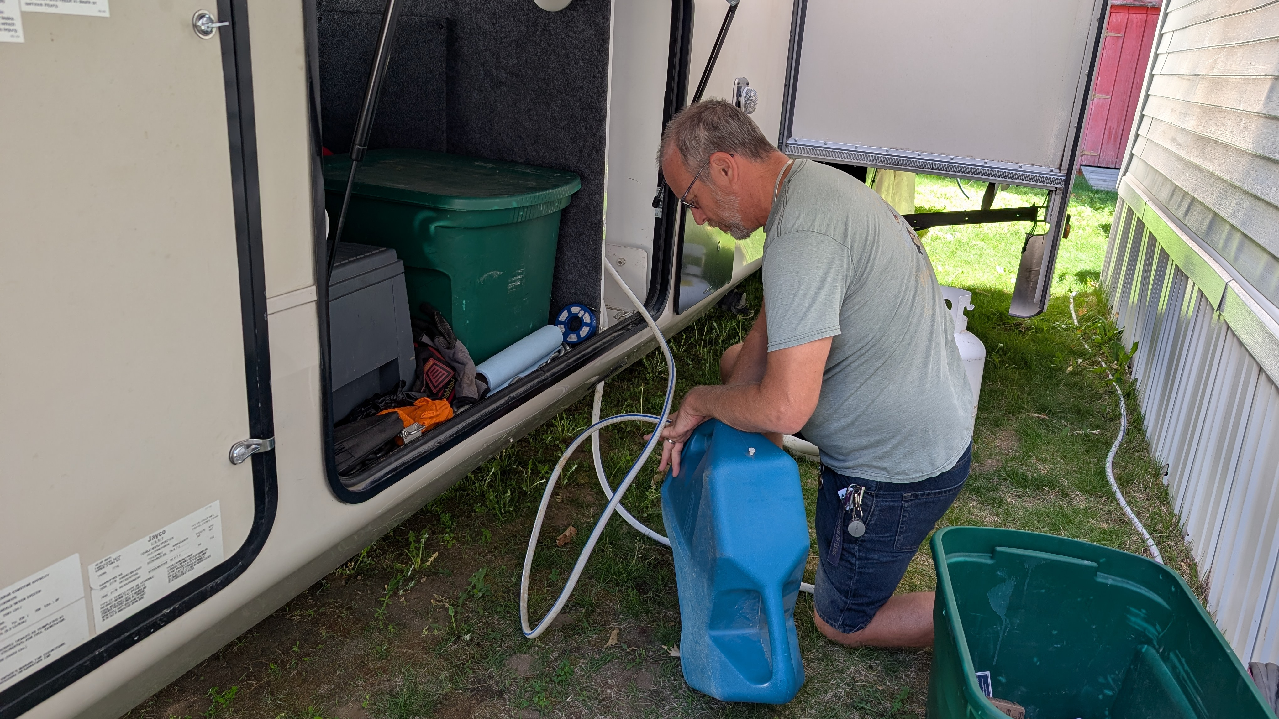 Bob kneeling over a 7-gallon container connected to a fifth-wheel RV with a hose