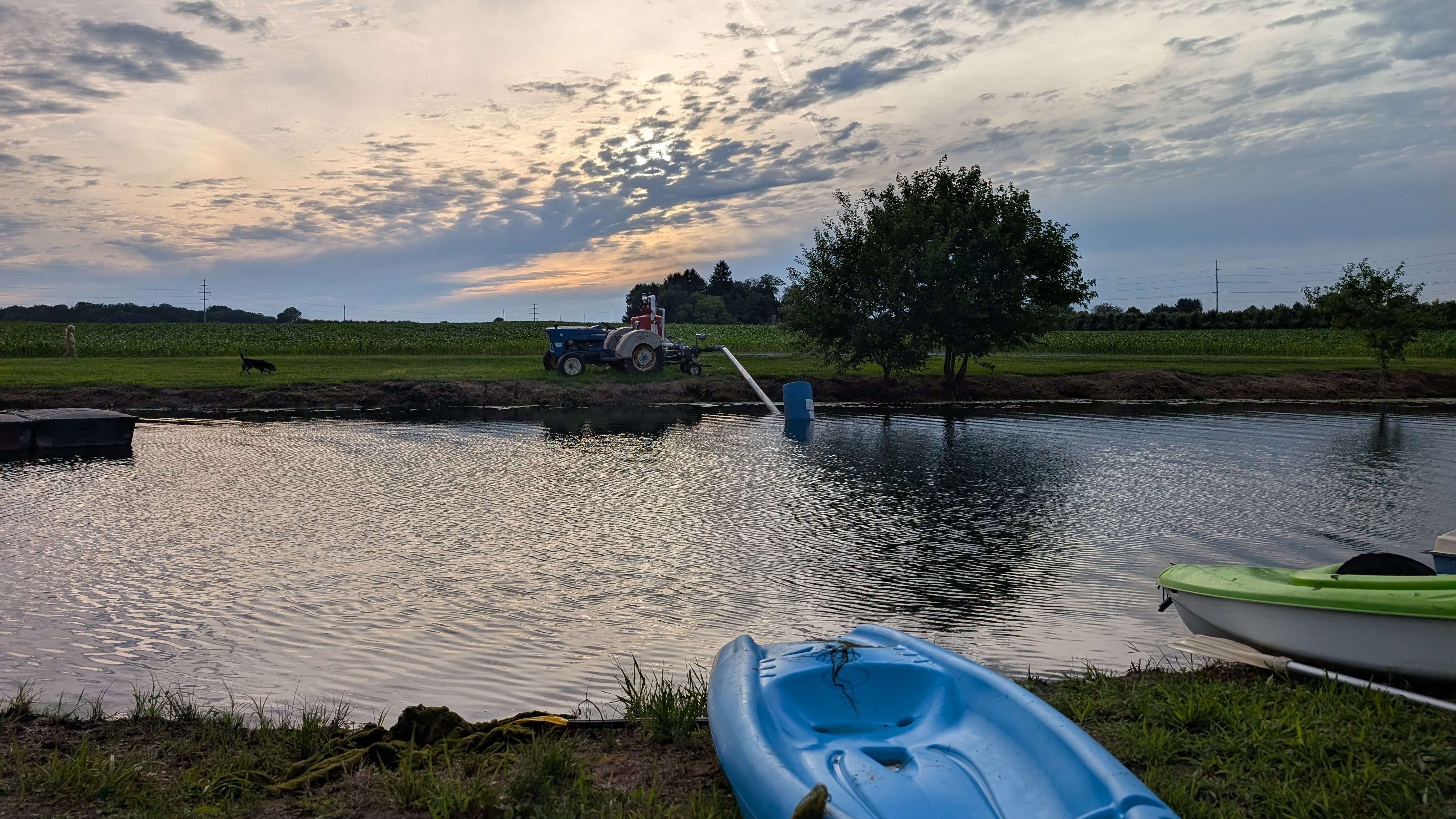 A farm pond with kayaks in the foreground and  a tractor in the background at sunset
