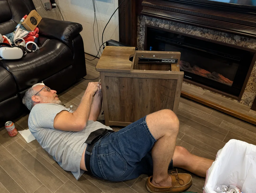 A man on his back on an RV floor repairing a table