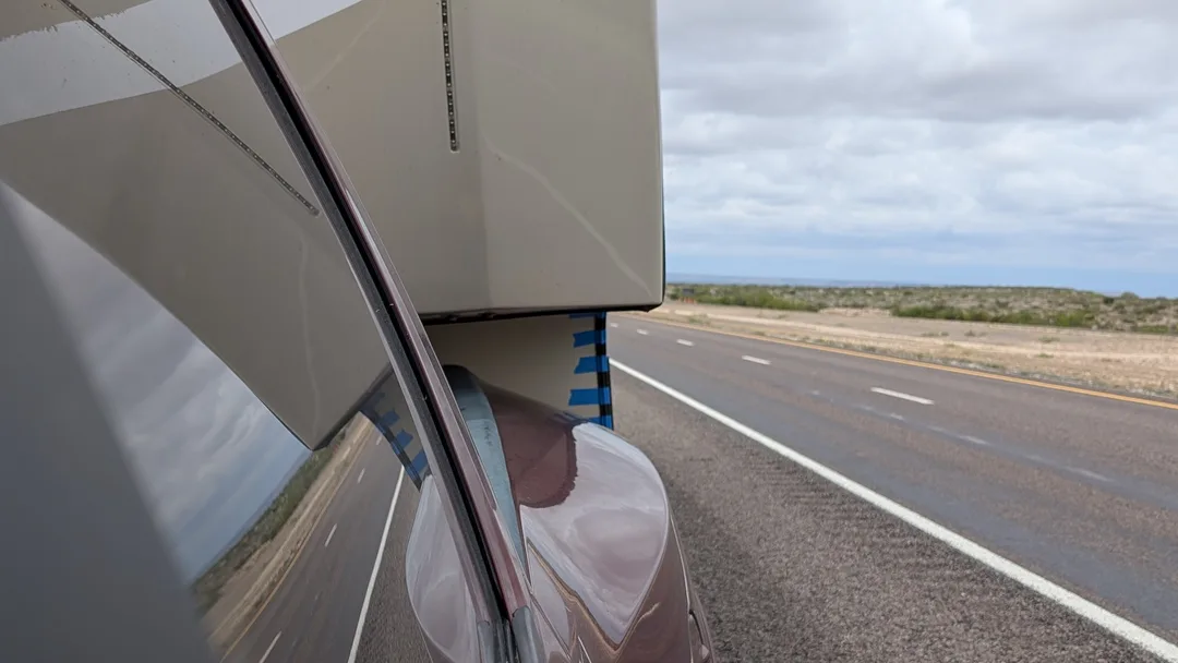 Driver's view of a fifth wheel connected to a truck showing strips of blue tape over trim