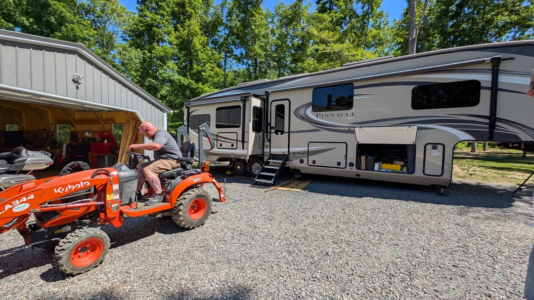 Man on an orange tractor on the side of a fifth wheel RV